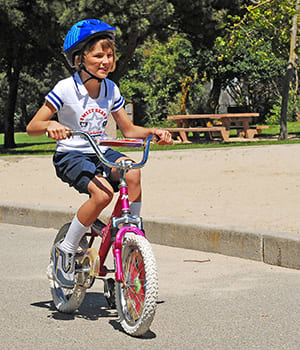 Child wearing helmet  riding bicycle in park.