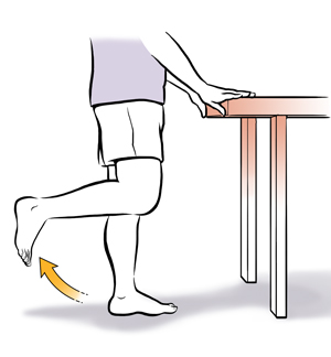 Person from waist down with hands on a table bending leg up at the knee. 
