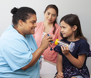 Health care provider showing girl how to use metered-dose inhaler with spacer and mask.